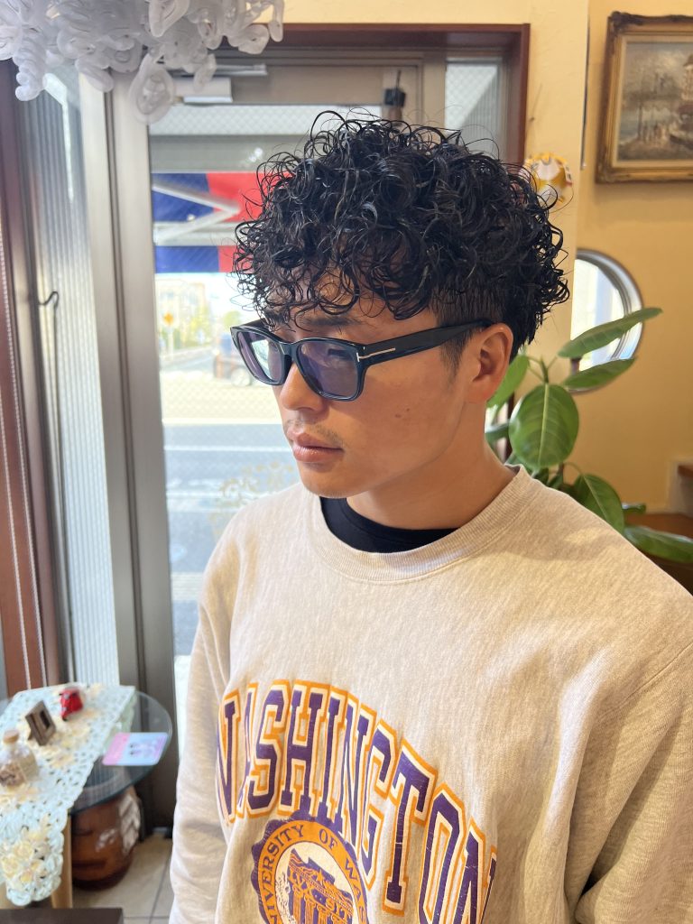 刈り上げベースにツイストスパイラルパーマをかけたメンズヘア。束感と動きが強調された男らしいスタイル。